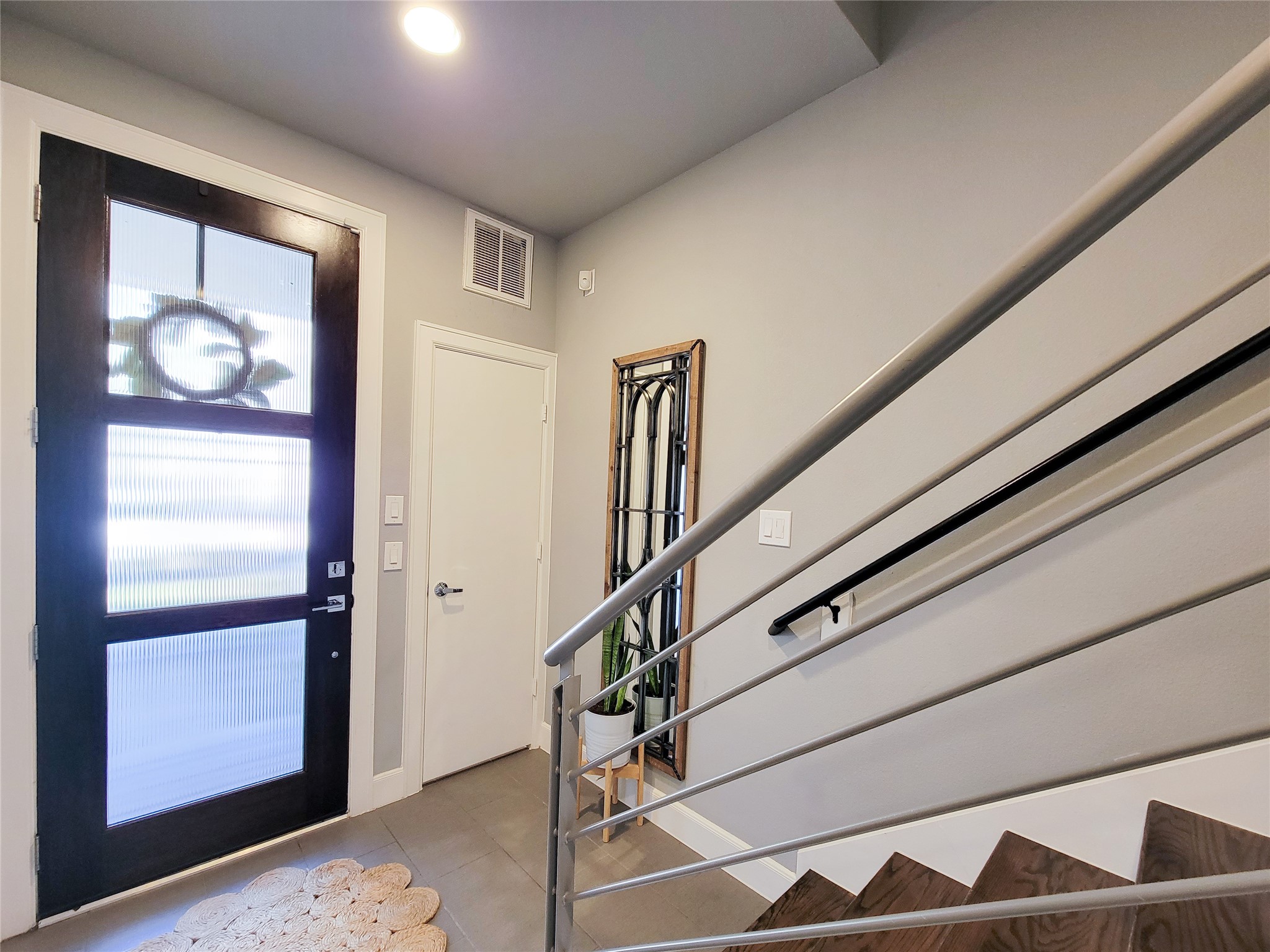 1705 Eado Point Lane Houston, TX 77003 - Photo 6 of 50 Bright entryway with modern design features, including a frosted glass front door, sleek staircase with metal railings, and neutral gray walls.