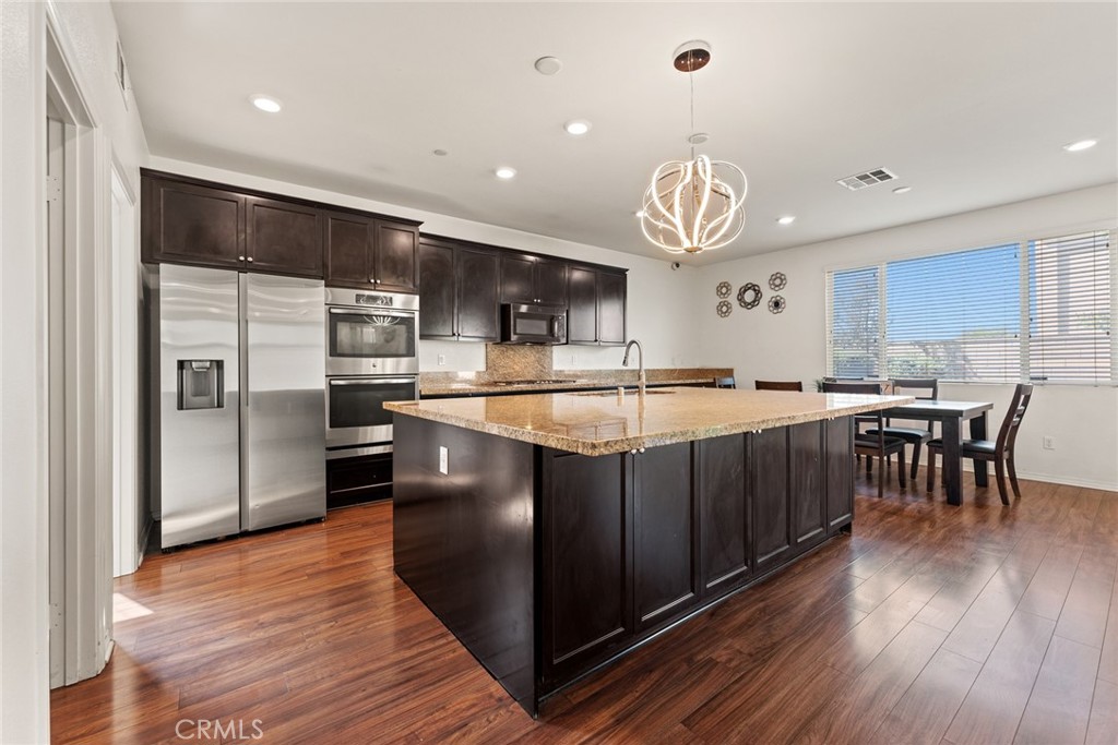 8022-8022 Sea Salt Avenue Fontana, CA 92336 - Photo 10 of 35 a kitchen with stainless steel appliances granite countertop a refrigerator a sink dishwasher a stove and a dining table with wooden floor