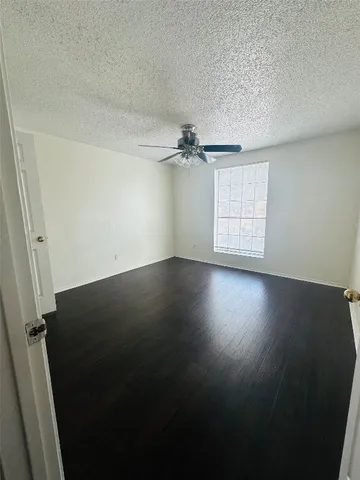 an empty room with wooden floor fan and windows