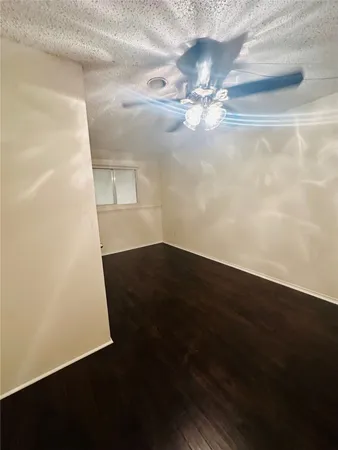 a view of an empty room with wooden floor and fan