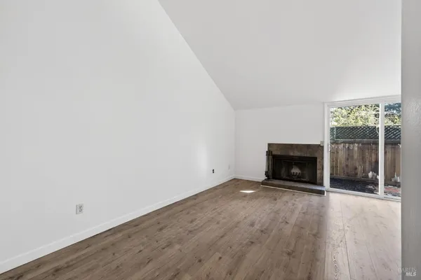 a view of an empty room with wooden floor fireplace and a window