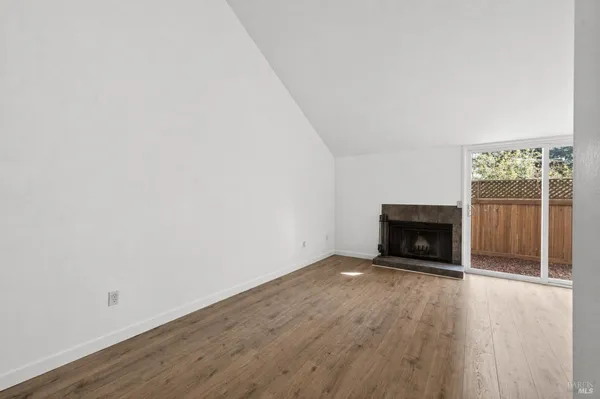 a view of an empty room with wooden floor fireplace and a window