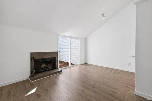 a view of an empty room with wooden floor fireplace and a window