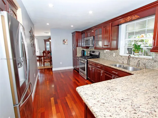 a kitchen with stainless steel appliances granite countertop a refrigerator a sink dishwasher a stove and white countertops with wooden floor