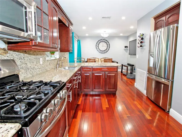 a kitchen with stainless steel appliances granite countertop a stove a sink dishwasher and a refrigerator with wooden floor