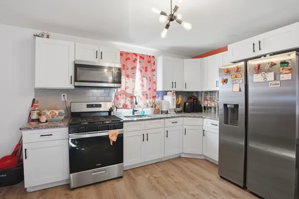 a kitchen with stainless steel appliances granite countertop a refrigerator a stove a sink dishwasher and white cabinets with wooden floor