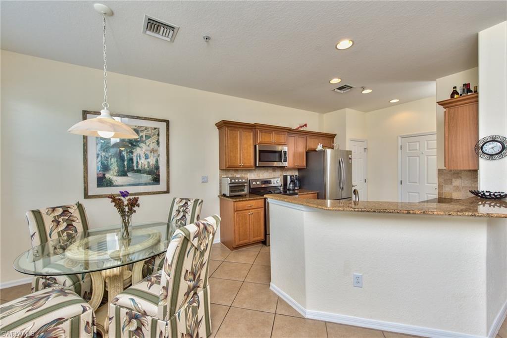 12859 Carrington Circle, Unit 3202 Naples, FL 34105 - Photo 3 of 28 a kitchen with stainless steel appliances granite countertop a sink a stove a dining table and chairs