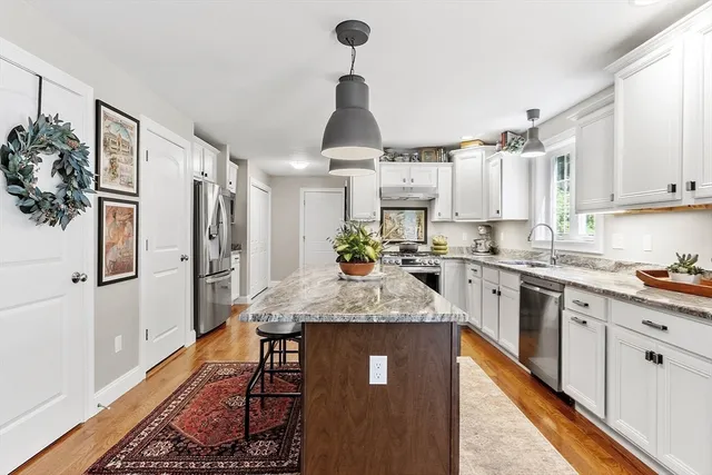 a kitchen with stainless steel appliances granite countertop a refrigerator a sink dishwasher a stove and white cabinets with wooden floor