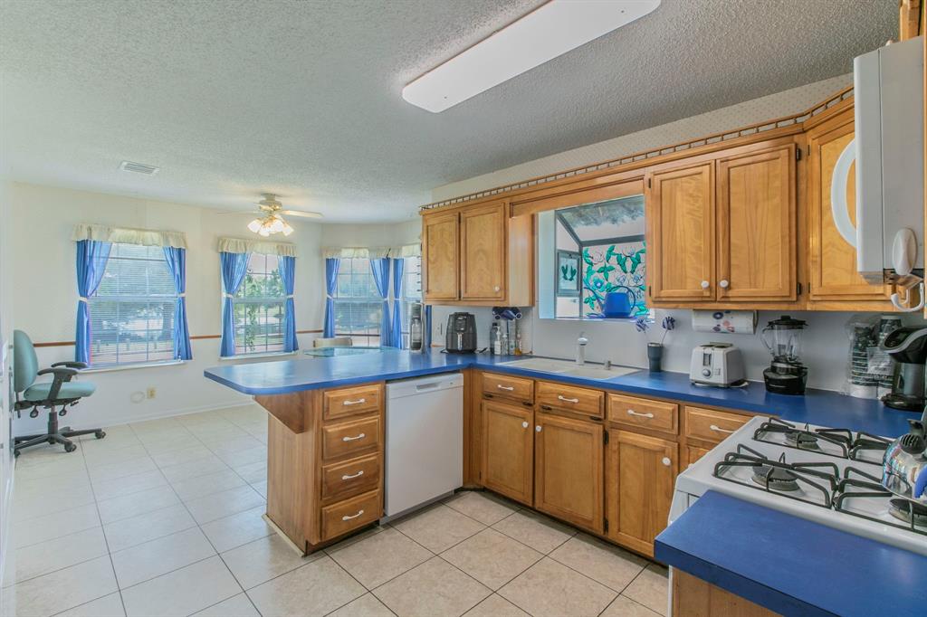 1936 Post Oak Drive Waco, TX 76705 - Photo 6 of 33 Kitchen featuring brown cabinets, a peninsula, a textured ceiling, white appliances, and light tile patterned flooring