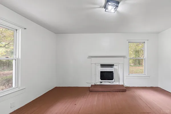 an empty room with wooden floor fireplace and windows