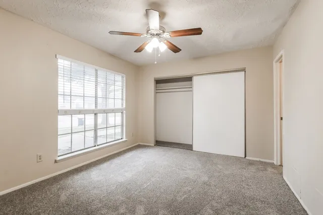 an empty room with chandelier fan and windows