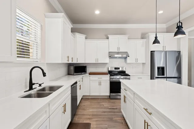 a kitchen with stainless steel appliances kitchen island granite countertop a refrigerator a stove and white cabinets with wooden floor