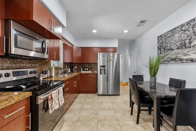 a kitchen with stainless steel appliances granite countertop a refrigerator a stove a sink a dining table and chairs