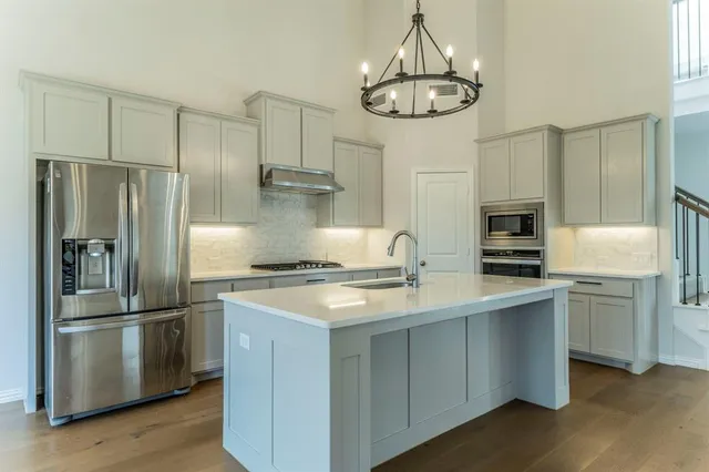 a kitchen with stainless steel appliances granite countertop a refrigerator a sink dishwasher a stove and a refrigerator with wooden floor