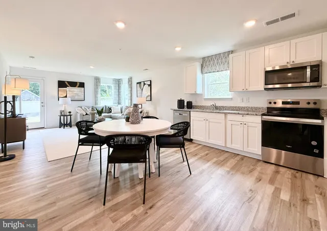 a kitchen with stainless steel appliances granite countertop a stove a sink a microwave a dining table and chairs with wooden floor