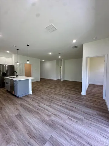 a view of an empty room with wooden floor and kitchen view