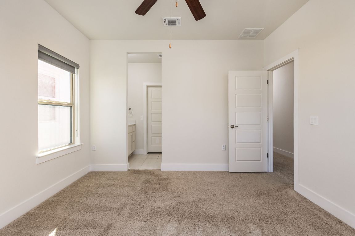 2401 McBee Street Austin, TX 78723 - Photo 27 of 36 Unfurnished bedroom with light colored carpet, connected bathroom, and a ceiling fan