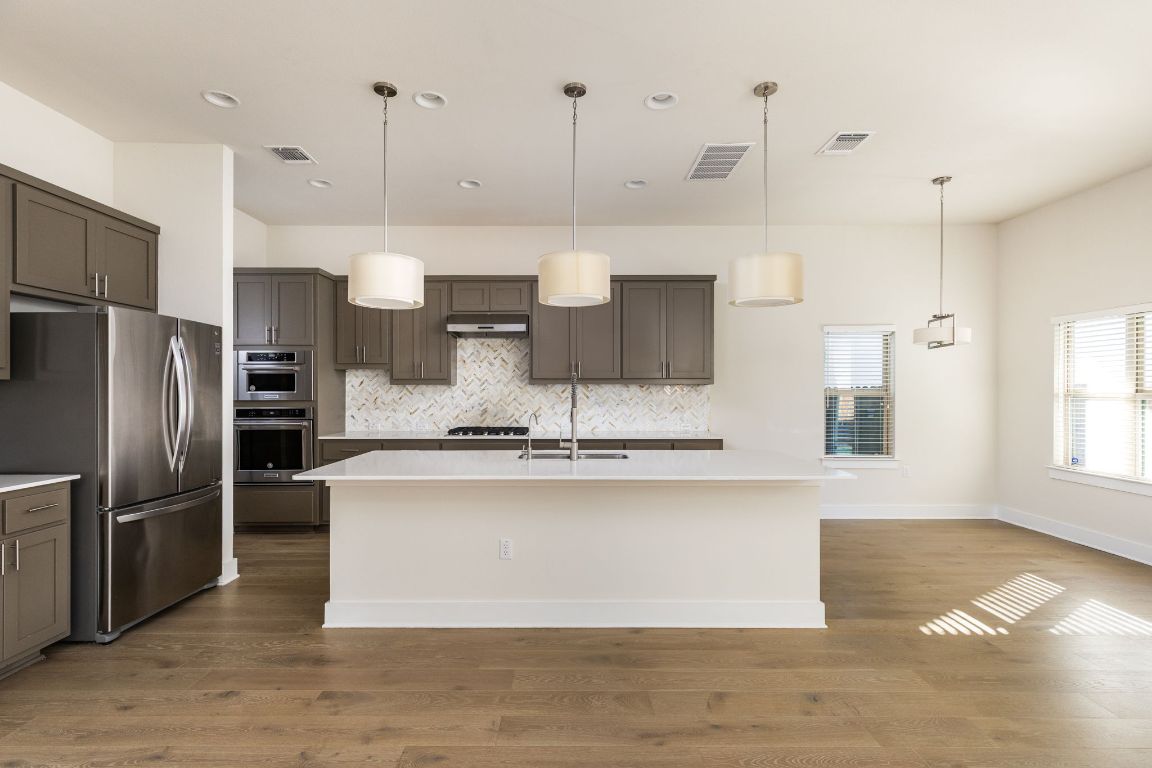 2401 McBee Street Austin, TX 78723 - Photo 8 of 36 Kitchen with pendant lighting, freestanding refrigerator, tasteful backsplash, a kitchen island with sink, and dark wood finished floors