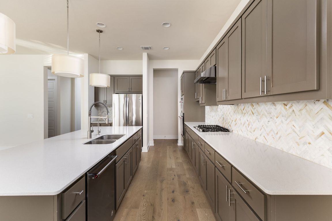 2401 McBee Street Austin, TX 78723 - Photo 10 of 36 Kitchen featuring a center island with sink, decorative light fixtures, light wood-style floors, appliances with stainless steel finishes, and light stone countertops