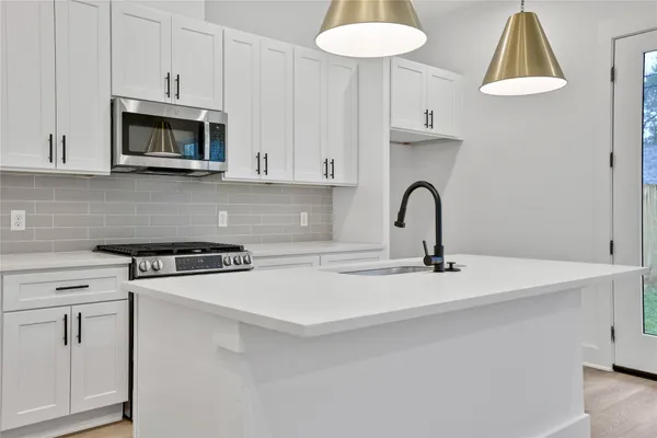 a kitchen with stainless steel appliances a stove a sink a microwave a refrigerator and white cabinets