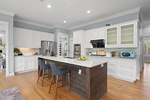 a kitchen with a sink a stove a refrigerator and white cabinets with wooden floor