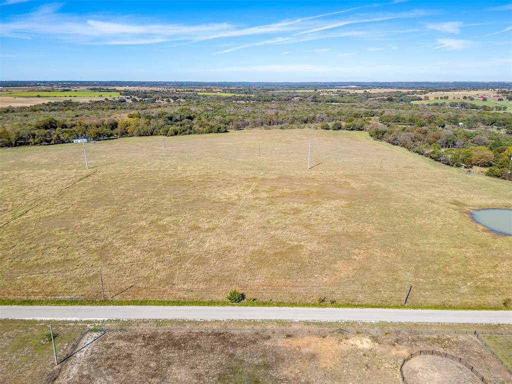 0 County Road 410 Road Alvarado, TX 76009 - Photo 4 of 12 Expansive open land featuring a natural pond, bordering a paved road, and surrounded by mature tree lines