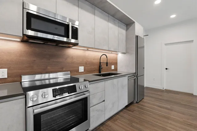 a kitchen with stainless steel appliances a stove a microwave oven cabinets and a wooden floor