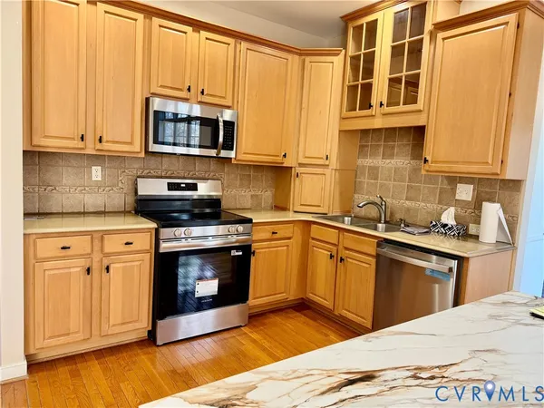 a large kitchen with stainless steel appliances granite countertop a stove top oven a sink dishwasher a dining table and chairs with wooden floor