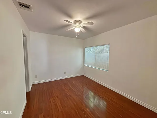an empty room with wooden floor fan and windows