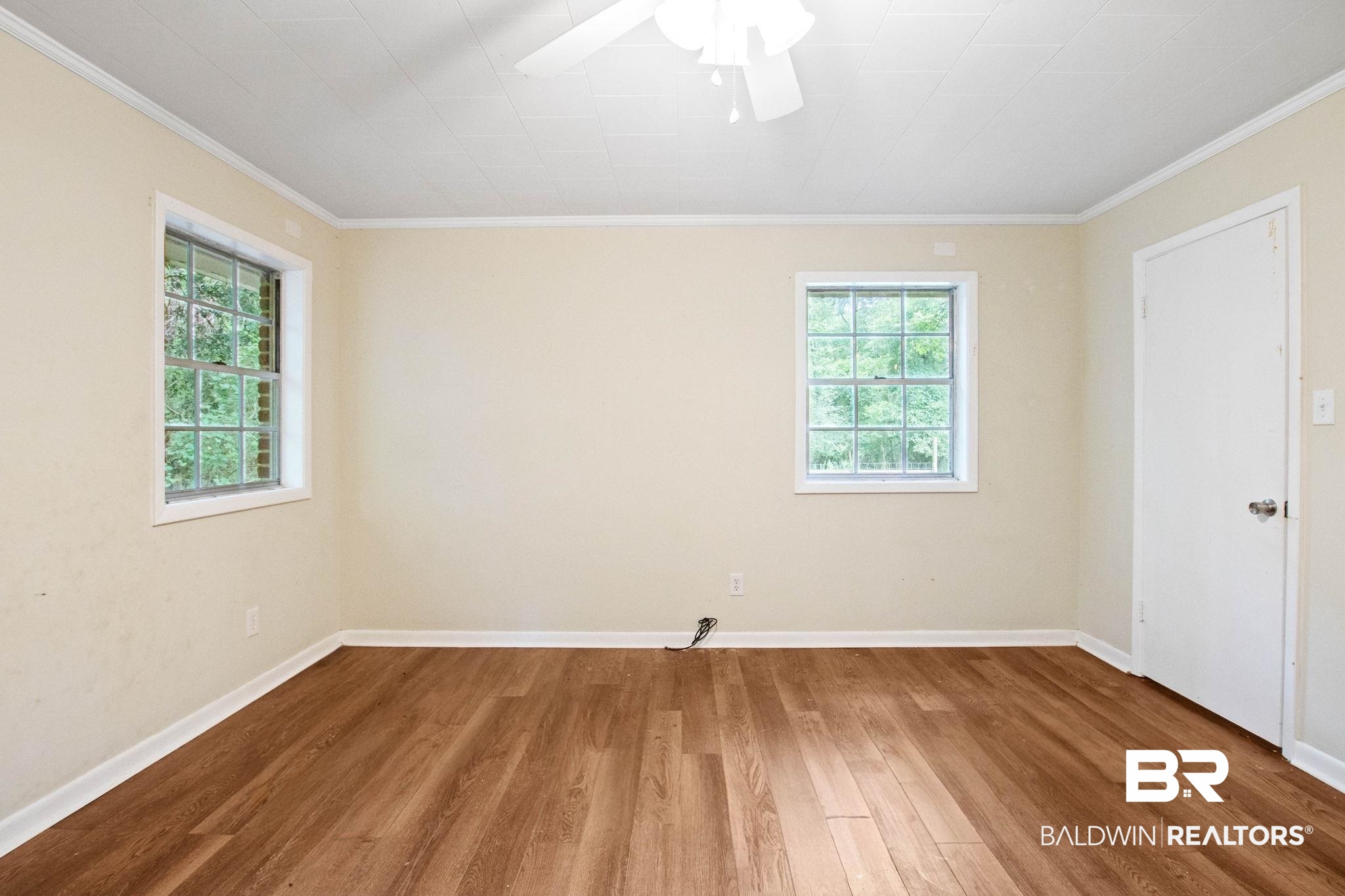 384 Old Bratt Road Atmore, AL 36502 - Photo 35 of 64 Room featuring wood-finish flooring, two windows with exterior foliage, a ceiling fan, and a white interior door