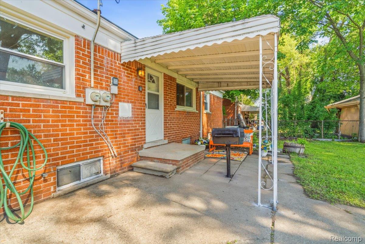 11802 Columbia Street Redford, MI 48239 - Photo 34 of 39 Rear concrete patio with a full-length awning, brick exterior, white screen door, and a grass lawn