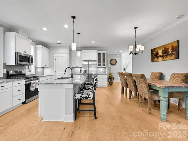 a open kitchen with granite countertop a stove a sink a dining table and chairs with wooden floor