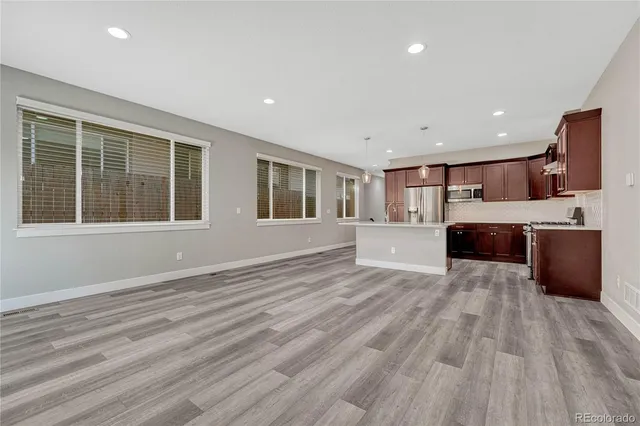 a view of living room kitchen with stainless steel appliances wooden floor and large window