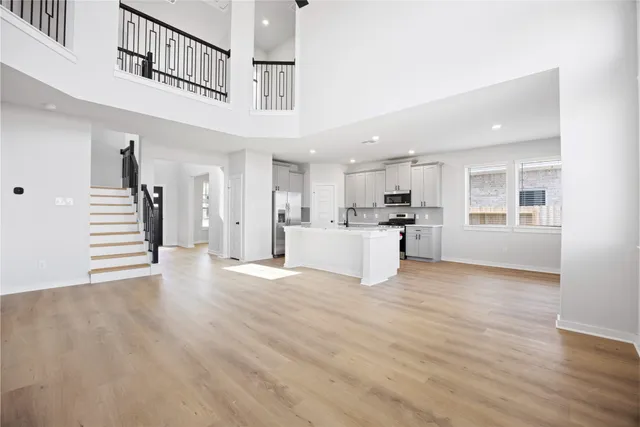 a view of an empty room and kitchen with wooden floor