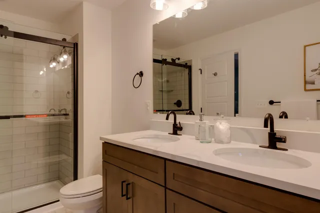 a bathroom with a double vanity sink toilet mirror and shower