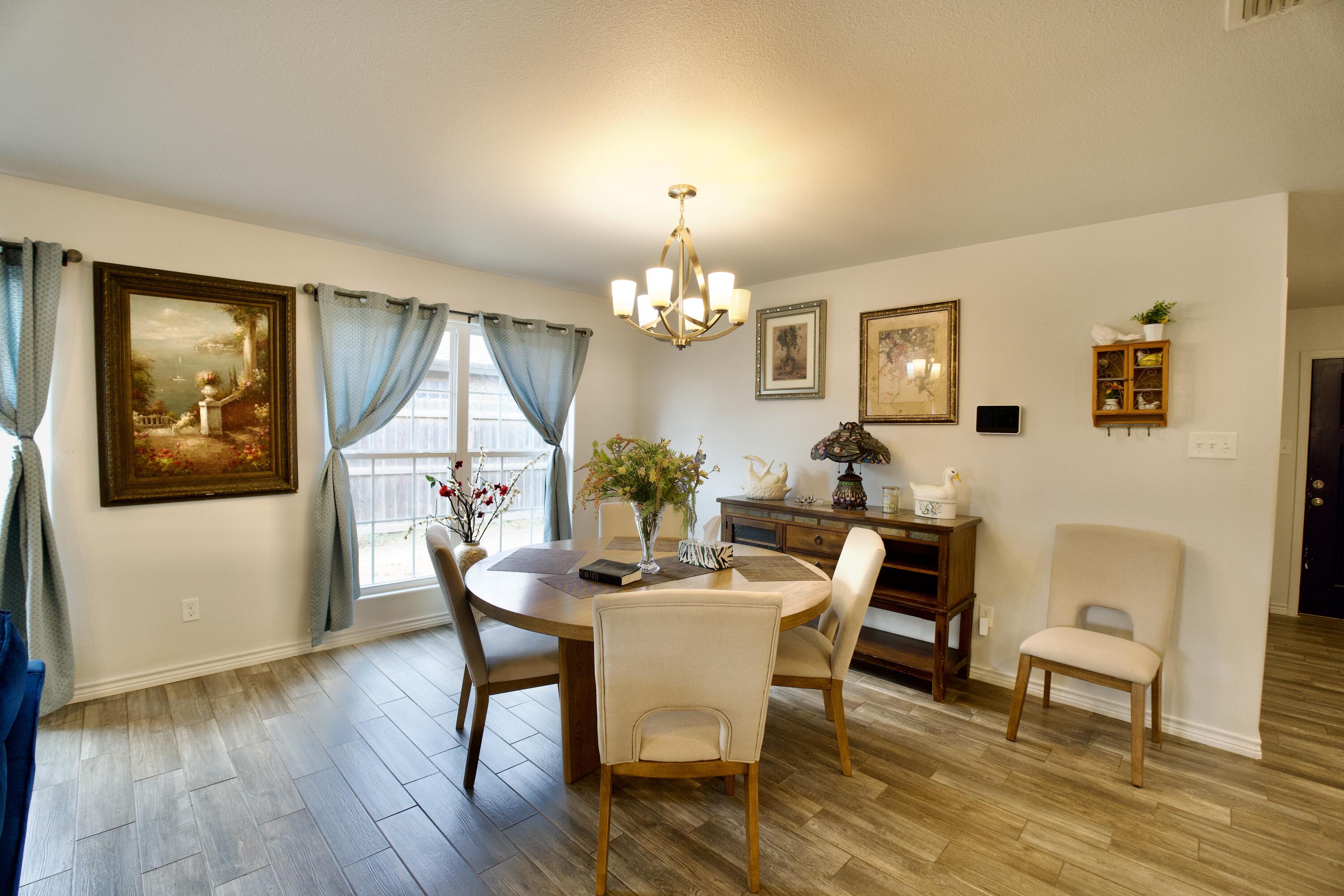 8813 17th Street Lubbock, TX 79416 - Photo 6 of 20 a dining room with wooden floor a chandelier a wooden table and chairs