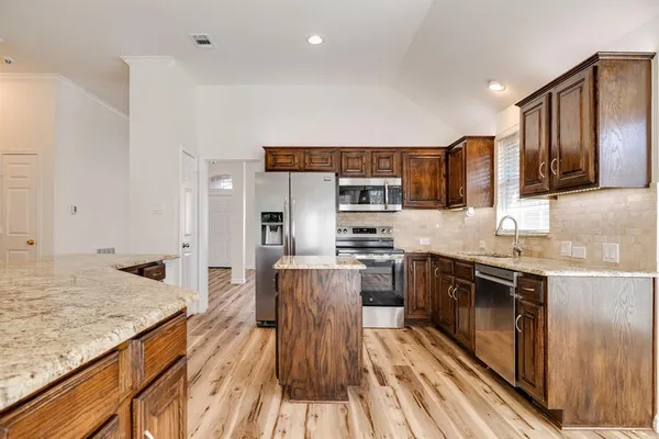 a kitchen with stainless steel appliances granite countertop a stove top oven a sink dishwasher and wooden cabinets with wooden floor