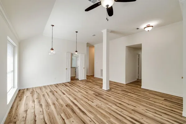 a view of an empty room with wooden floor and a ceiling fan