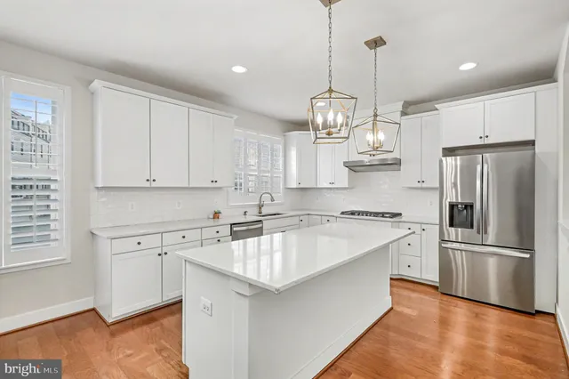 a kitchen with stainless steel appliances granite countertop a sink dishwasher a refrigerator and white cabinets with wooden floor