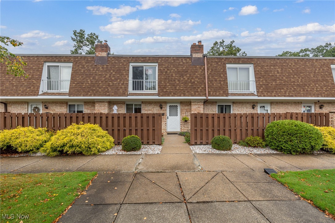 Front of property featuring mansard roof, a shingled roof, a fenced front yard, and brick siding