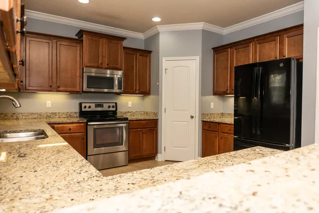 a kitchen with granite countertop wooden cabinets a refrigerator stove top oven a sink and dishwasher