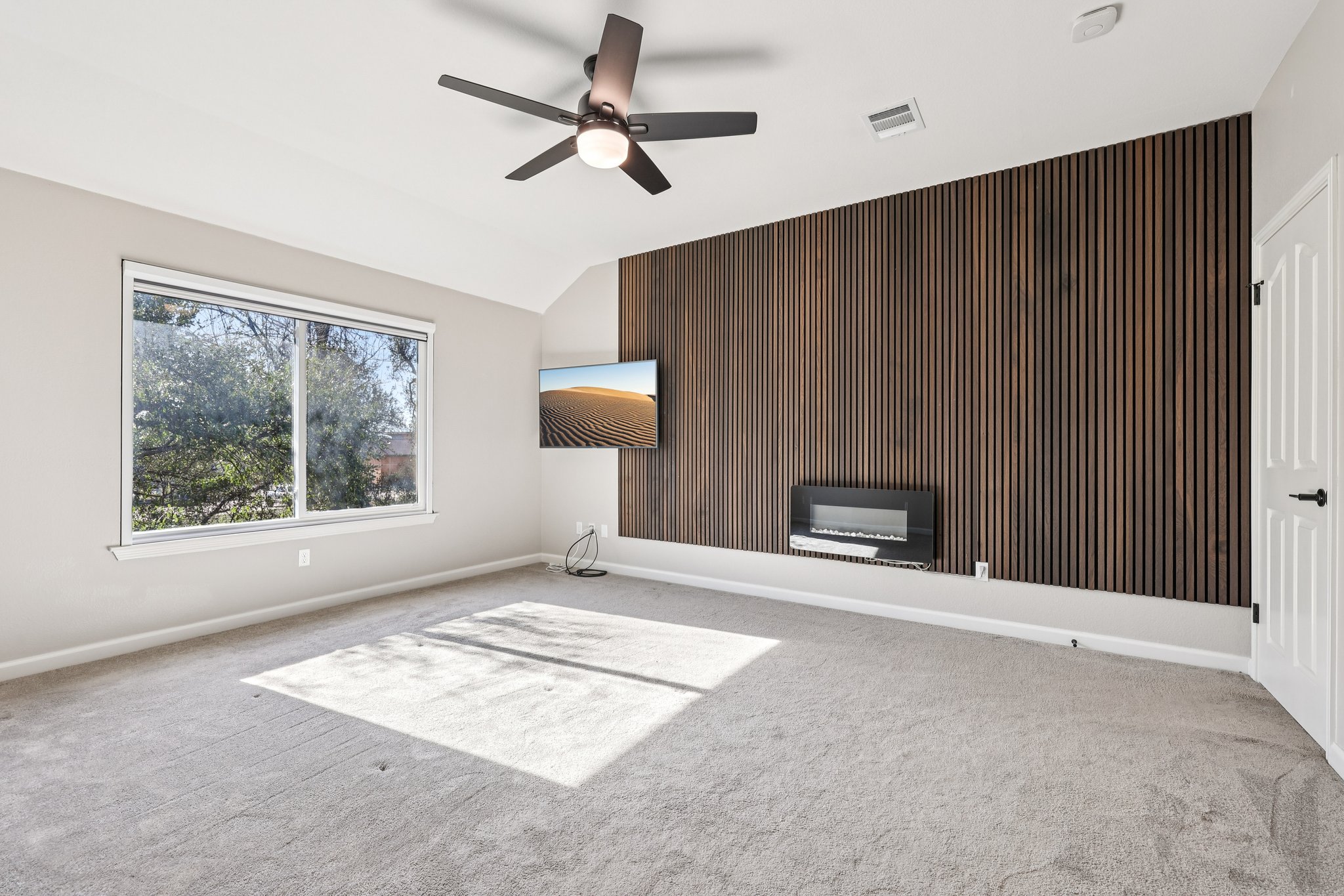 12717 Machete Trail Austin, TX 78729 - Photo 14 of 32 Unfurnished living room featuring wooden walls, an accent wall, carpet flooring, a ceiling fan, and vaulted ceiling