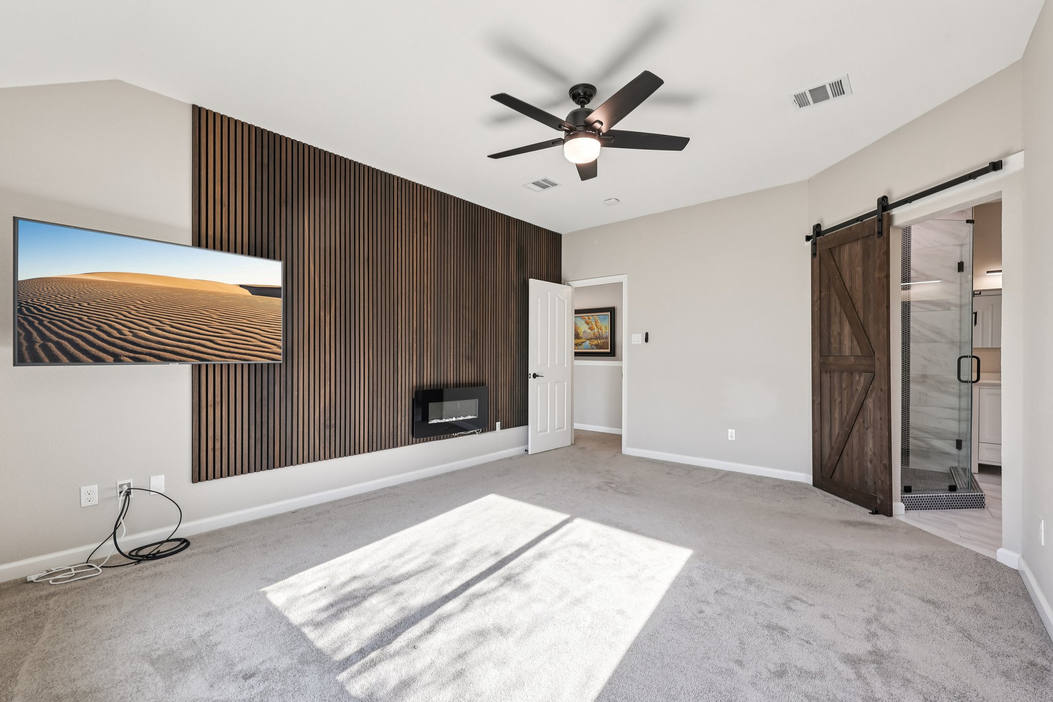 12717 Machete Trail Austin, TX 78729 - Photo 15 of 32 Unfurnished bedroom featuring wood walls, a barn door, light carpet, ceiling fan, and an accent wall