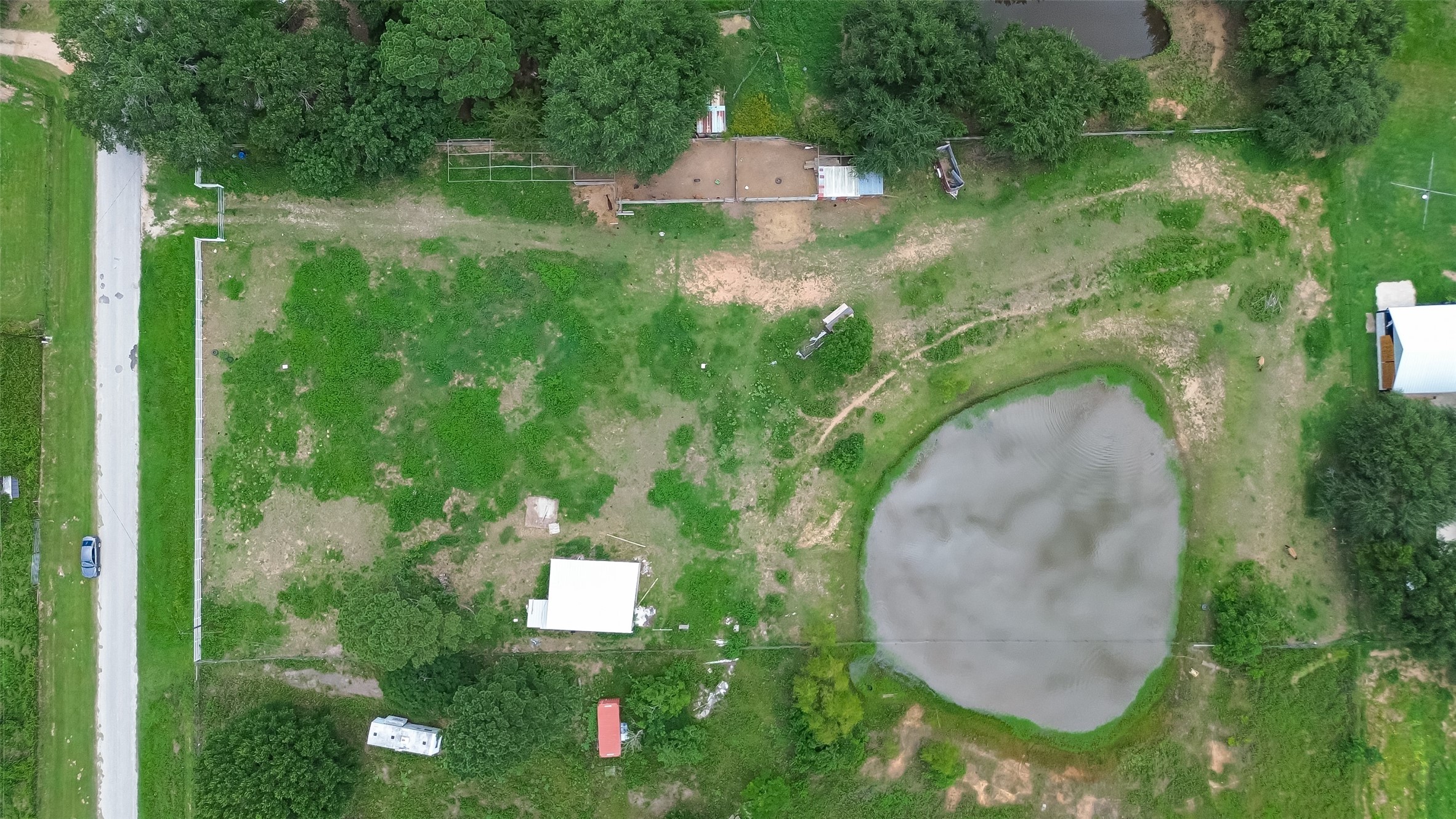 35535 Windmill Road Hempstead, TX 77445 - Photo 2 of 41 This aerial photo shows a spacious plot with lush green areas, a small pond, and some structures, ideal for rural living or development. The property is bordered by a road and features mature trees providing natural privacy.