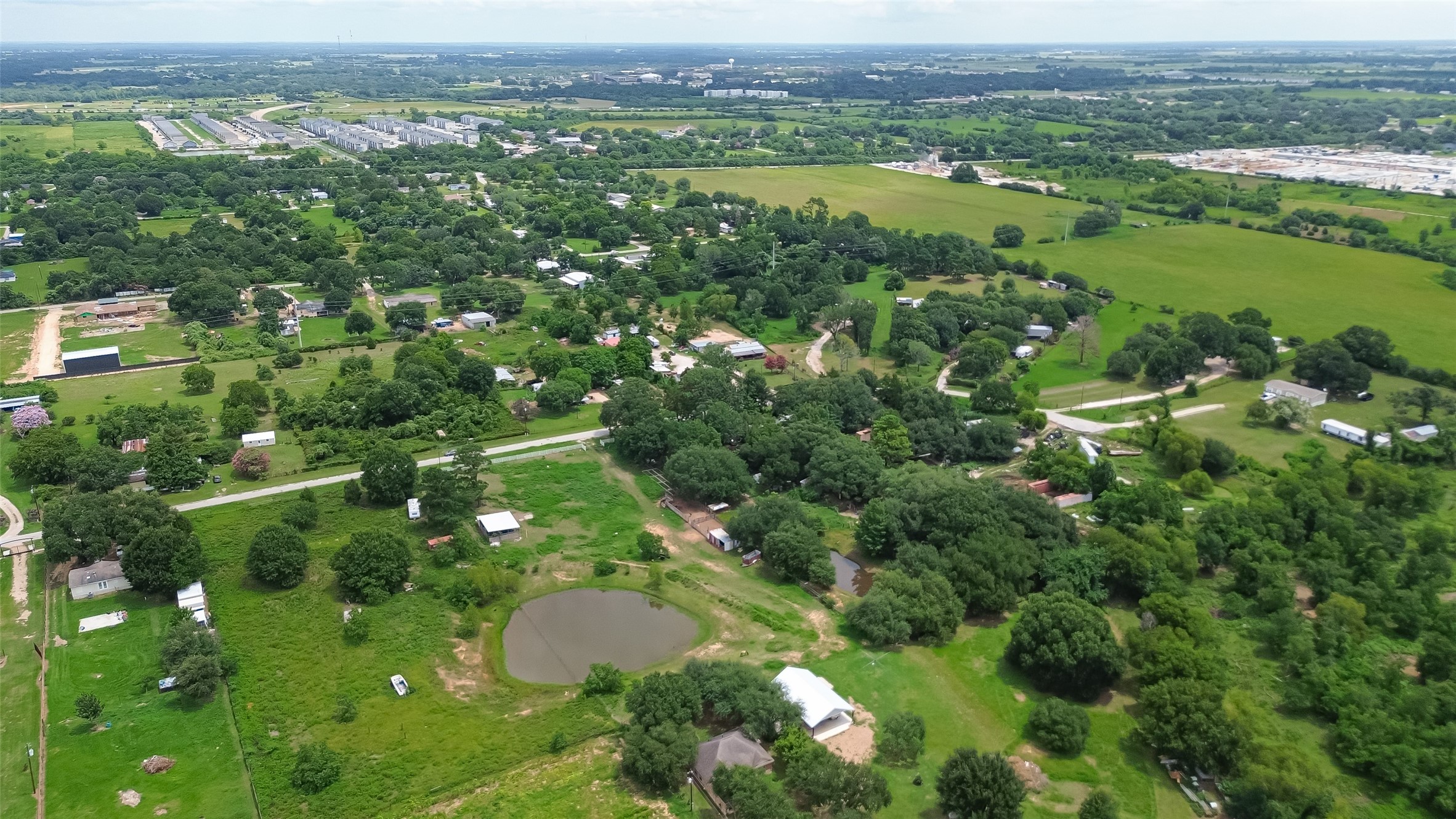 35535 Windmill Road Hempstead, TX 77445 - Photo 30 of 41 This aerial view showcases a serene, rural neighborhood with lush greenery and scattered homes. The landscape features open fields, a small pond, and winding roads, offering a peaceful country living experience with ample space and natural beauty.