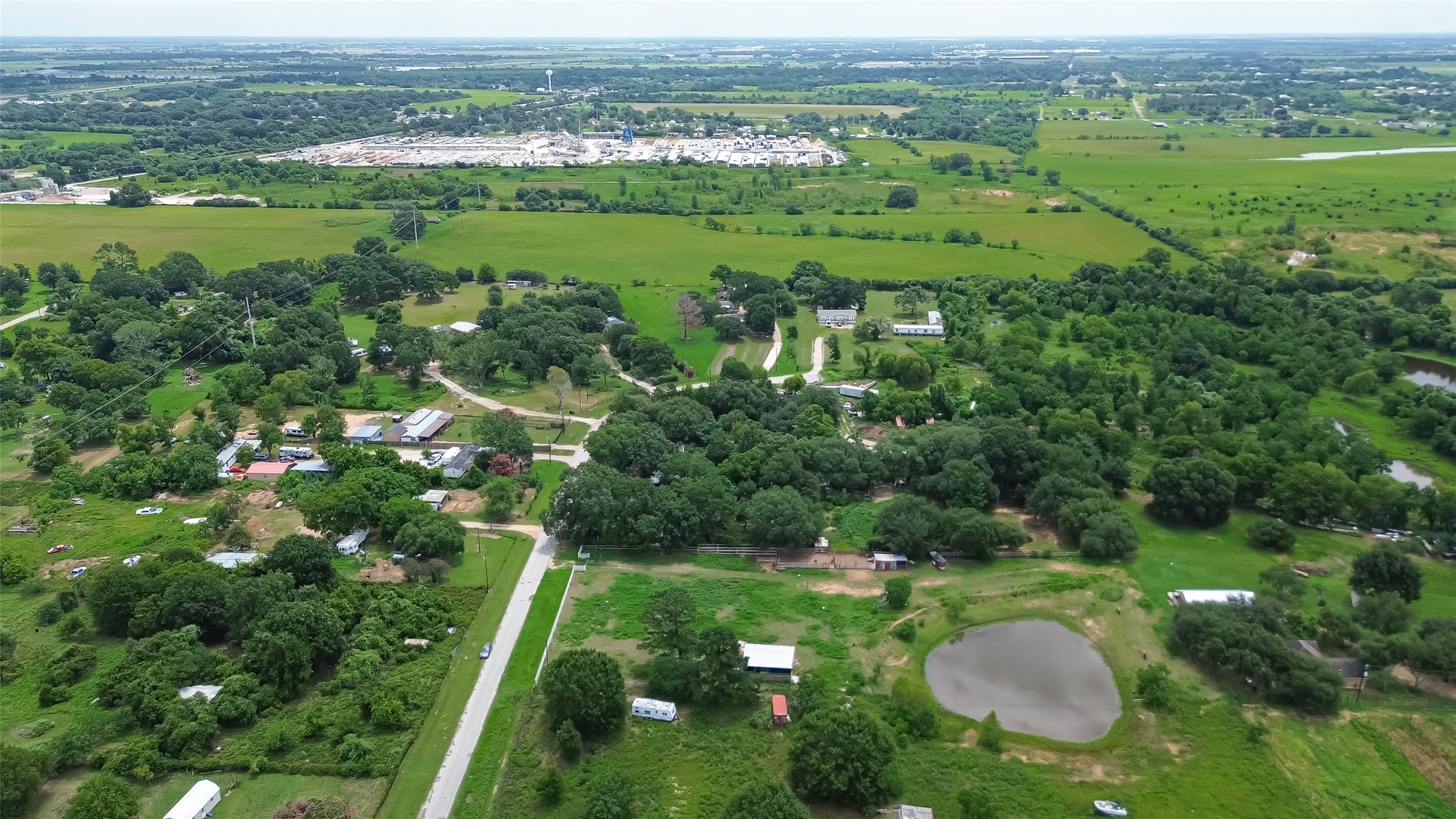 35535 Windmill Road Hempstead, TX 77445 - Photo 33 of 41 This aerial photo shows a spacious rural setting with lush greenery, scattered homes, and a small pond. The area offers expansive views and a peaceful environment, ideal for those seeking a country lifestyle.