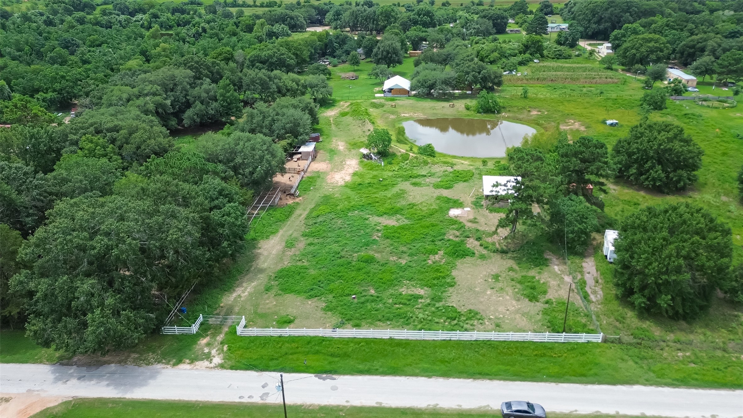 35535 Windmill Road Hempstead, TX 77445 - Photo 36 of 41 This aerial view showcases a spacious rural property with lush greenery, a pond, and several outbuildings. A white fence lines the front, providing a charming entrance from a quiet road. Ideal for those seeking tranquility and open space.