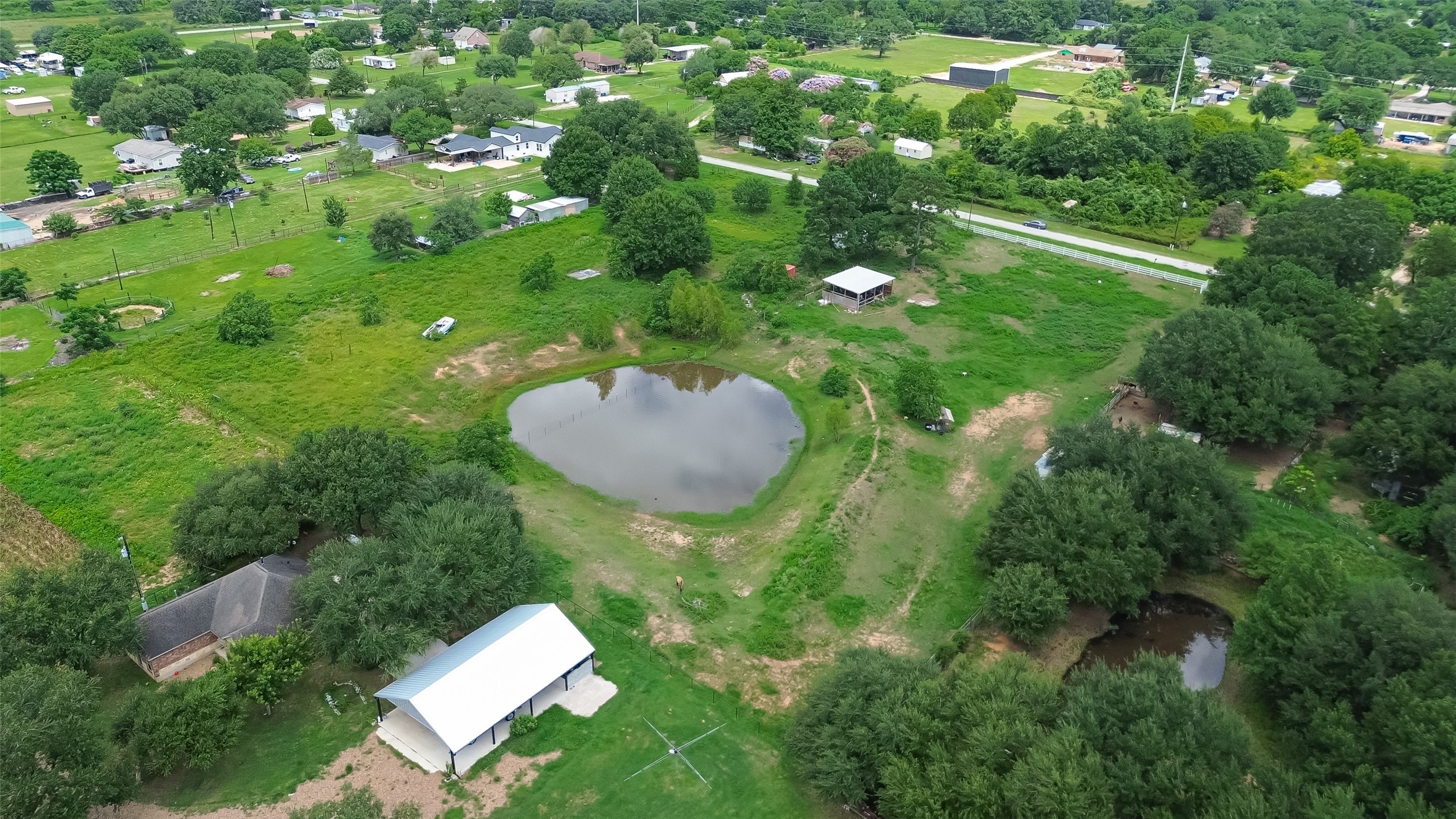 35535 Windmill Road Hempstead, TX 77445 - Photo 39 of 41 This aerial photo showcases a spacious rural property with lush greenery, a central pond, and several structures, including a house and a large outbuilding. The area is surrounded by trees and open fields, offering a peaceful, private setting ideal for country living.