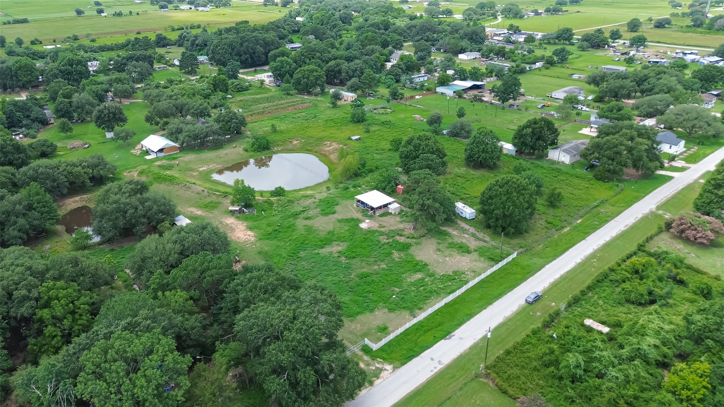 35535 Windmill Road Hempstead, TX 77445 - Photo 9 of 41 This aerial photo shows a spacious rural property with lush greenery, a small pond, and scattered trees. There are a few structures on the land and a road running alongside. It's a peaceful, open area ideal for someone seeking a countryside home.