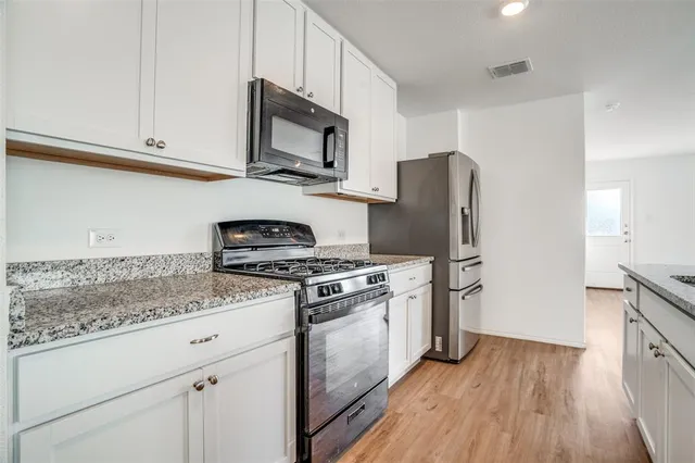 a kitchen with stainless steel appliances granite countertop a stove top oven a refrigerator a sink and dishwasher with wooden floor